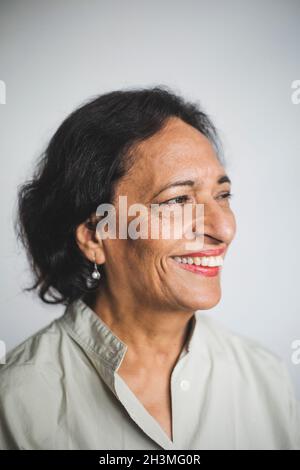 Sorridente donna anziana che guarda via contro il muro Foto Stock