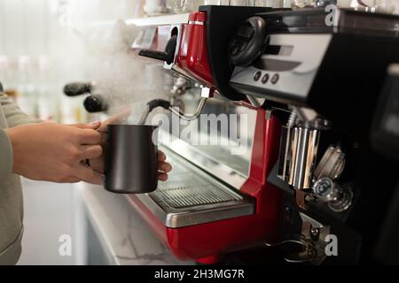 Barista maschio corto che fuma una bevanda calda in brocca durante il lavoro in un moderno caffè Foto Stock