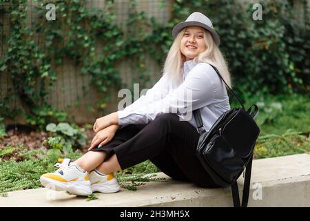 giovane donna sorridente bionda con zaino in mano al campus Foto Stock