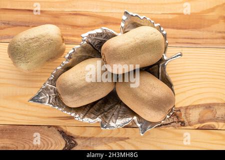Diversi kiwi dolci maturi in un vaso metallico su un tavolo di legno, primo piano, vista dall'alto. Foto Stock