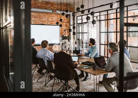 Imprenditrice femminile che parla con uomini d'affari e donne d'affari durante la riunione nella sala del consiglio Foto Stock