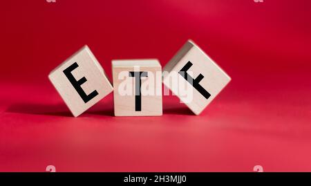 ETF, Exchange Traded Fund, un fondo mutuo di indice in tempo reale in grado di commerciare il mercato azionario, un cubo di legno con la parola ETF su sfondo rosso Foto Stock