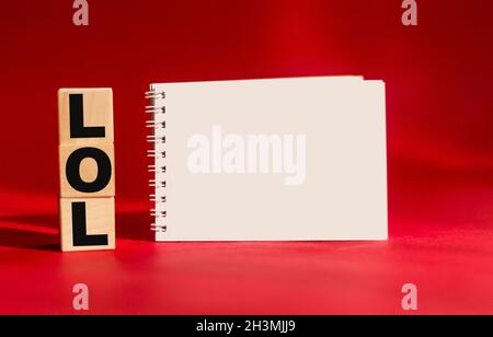 Cubi di legno con il testo LOL su sfondo rosso e con un blocco note per la scrittura Foto Stock