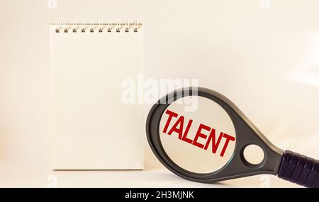 La parola Talent è scritta su una lente d'ingrandimento. Vicino a un blocco note per scrivere su uno sfondo bianco. Foto Stock
