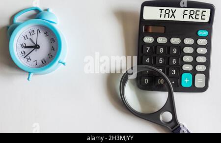 Calcolatrice con il testo Tax Free su sfondo bianco con sveglia e lente d'ingrandimento. Foto Stock