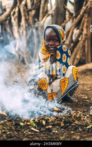 Tribù TOPOSA, SUDAN DEL SUD - 12 MARZO 2020: Bambino in stoffa ornamentale sorridente e guardando la macchina fotografica mentre si siede su haunches ne Foto Stock