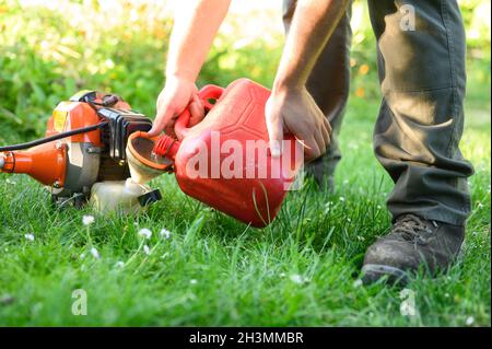 Taglierina a spazzola per il rifornimento del giardiniere in primo piano. Manutenzione degli attrezzi di giardinaggio. Cura del prato con decespugliatori. Foto Stock