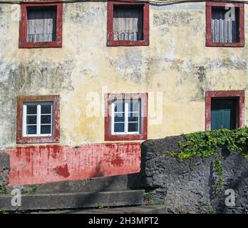 Facciata di una tipica casa spagnola dipinta in giallo sbiadito e rosso circondato da un muro grigio con piante a Funchal, T. Foto Stock