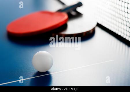 Due racchette da tennis e una palla bianca si trovano su un tavolo da tennis vicino alla rete. Attività ricreative attive e giocare a ping pong. Background sportivo. Foto Stock