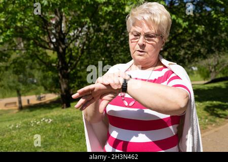 Donna anziana con occhiali che guardano il parco. Signora bionda anziana che controlla in tempo il giorno di sole all'aperto Foto Stock