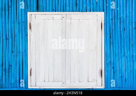 Finestra di legno bianco con porte arrugginite su pareti di bambù blu di una capanna sulla spiaggia nell'isola di Koh Phangan, Thailandia. Orari di apertura Foto Stock