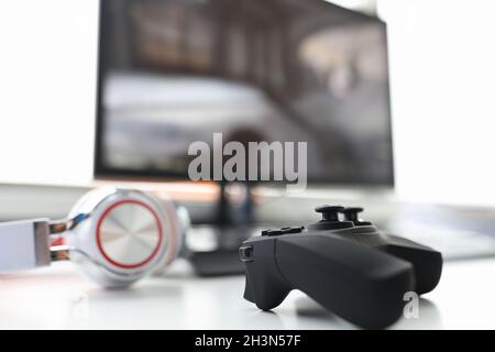 Joystick di gioco con cuffie giacciono sul tavolo con il primo piano del monitor del computer Foto Stock