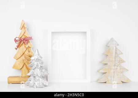 Mock su cornice bianca con decorazioni in legno albero di Natale su una mensola. Cornice verticale contro una parete bianca. Foto Stock