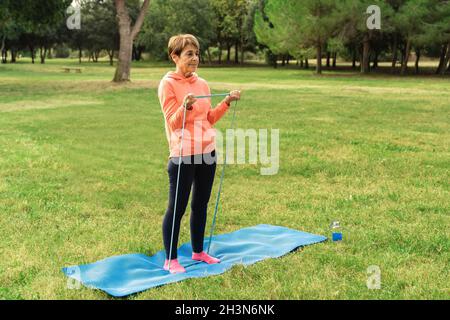 Donna anziana che fa pilates allenamento routine all'aperto al parco della città - Focus on Face Foto Stock