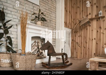 In una stanza accanto al caminetto si trova un cavallo in legno dondolante. Vicino cesti di vimini con piante. Foto di alta qualità Foto Stock