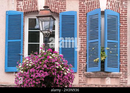 Finestre di una casa francese in mattoni a Honfleur, in Normandia, con persiane di legno blu e composizione di fiori Foto Stock