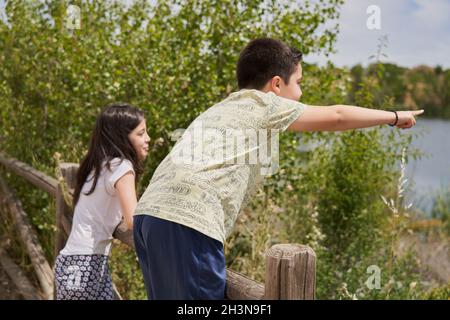 I bambini che puntano guardando felice appoggiandosi su una recinzione di legno in un parco Foto Stock