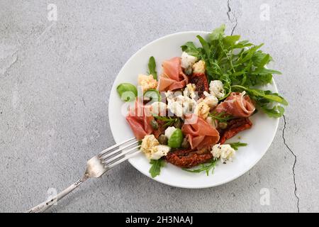 Rucola per insalata, prosciutto di Parma con pomodori secchi, fette di mozzarella, crostini, capperi, olio condito Foto Stock