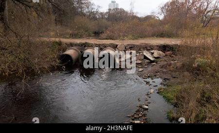 Tubi per rifiuti in calcestruzzo. Flussi di acqua fluiscono attraverso tubi di calcestruzzo. Corpo inquinato di acqua nel parco. Tiro dal drone. Fotografia aerea. Foto Stock