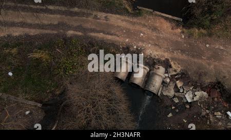 Tubi per rifiuti in calcestruzzo. Flussi di acqua fluiscono attraverso tubi di calcestruzzo. Corpo inquinato di acqua nel parco. Tiro dal drone. Fotografia aerea. Foto Stock