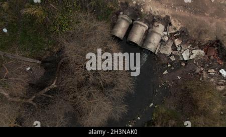 Tubi per rifiuti in calcestruzzo. Flussi di acqua fluiscono attraverso tubi di calcestruzzo. Corpo inquinato di acqua nel parco. Tiro dal drone. Fotografia aerea. Foto Stock