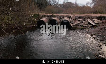 Tubi per rifiuti in calcestruzzo. Flussi di acqua fluiscono attraverso tubi di calcestruzzo. Corpo inquinato di acqua nel parco. Tiro dal drone. Fotografia aerea. Foto Stock