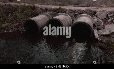 Tubi per rifiuti in calcestruzzo. Flussi di acqua fluiscono attraverso tubi di calcestruzzo. Corpo inquinato di acqua nel parco. Tiro dal drone. Fotografia aerea. Foto Stock