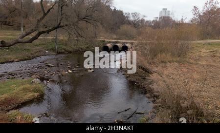 Tubi per rifiuti in calcestruzzo. Flussi di acqua fluiscono attraverso tubi di calcestruzzo. Corpo inquinato di acqua nel parco. Tiro dal drone. Fotografia aerea. Foto Stock