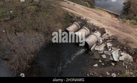 Tubi per rifiuti in calcestruzzo. Flussi di acqua fluiscono attraverso tubi di calcestruzzo. Corpo inquinato di acqua nel parco. Tiro dal drone. Fotografia aerea. Foto Stock