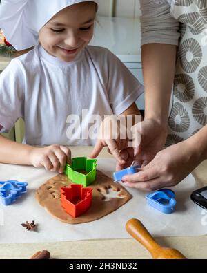 Felice madre e figlia che tagliano varie forme di biscotti in cucina. Mamma e figlia fanno biscotti di pan di zenzero a casa e Buon divertimento. Casa Foto Stock