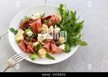 Rucola per insalata, prosciutto di Parma con pomodori secchi, fette di mozzarella, crostini, capperi, olio condito Foto Stock