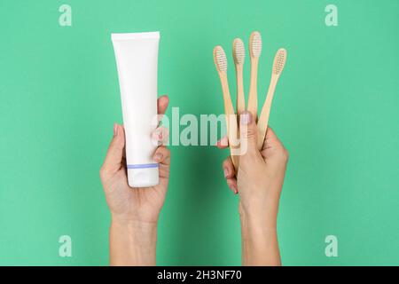 Spazzolini di bambù e un tubo di dentifricio in mani femminili su uno sfondo di menta. Tendenze attuali nel consumo cosciente. Foto Stock