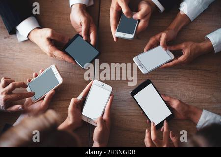 Gli impiegati lavorano sui telefoni. Concetto di riunione mobile. Primo piano delle mani umane utilizzando gli smartphone su un tavolo di legno. Vista dall'alto Foto Stock