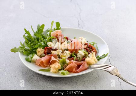 Rucola per insalata, prosciutto di Parma con pomodori secchi, fette di mozzarella, crostini, capperi, olio condito Foto Stock