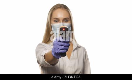 Infermiere medico in maschera di protezione sensore di puntamento termometro su fotocamera indossando bianco medico ospedale accappatoio. Giovani capelli biondi n Foto Stock