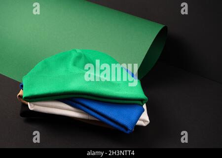 Una serie di cappelli di beanie in diversi colori blu, nero, bianco, verde impilati in un palo su un inusuale sfondo scuro. Pronto per il tuo layout Foto Stock