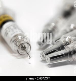Siringa con vaccino per combattere il coronavirus su un tavolo. Una goccia è sospesa dalla punta dell'ago. Foto Stock