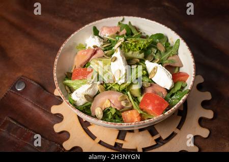 Una ciotola di insalata di verdure fresche con fette di salmone, mozzarella si trova su un tavolo coperto da uno straccio di pelle e una decora Foto Stock