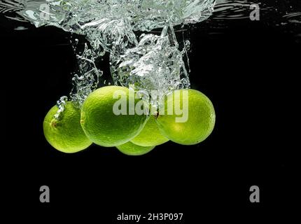 Citrus di lime spruzzi con le bolle in acqua isolato contro sfondo nero Foto Stock