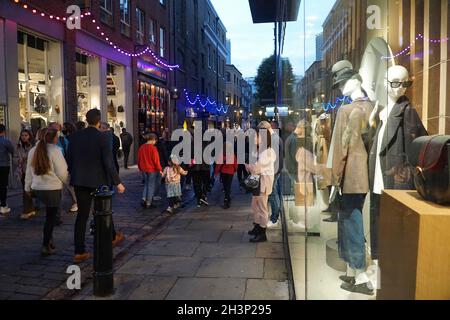 Londra, UK, 29 ottobre 2021: Mentre il crepuscolo cade a Covent Garden e nelle strade acciottolate circostanti, i turisti e gli amanti dello shopping godono di un incantesimo secco tra le docce a pioggia. Le campagne pubblicitarie volte a incoraggiare le persone a visitare Londra sembrano aver attirato molte visite familiari a metà termine e Londra ha attualmente un tasso di infezioni da covid inferiore rispetto ad altre aree del paese. Le decorazioni natalizie sono già in alto nella zona centrale del mercato. Anna Watson/Alamy Live News Foto Stock