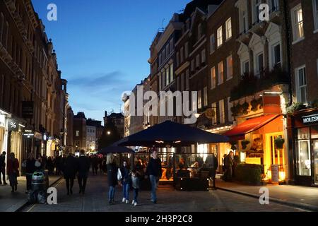 Londra, UK, 29 ottobre 2021: Mentre il crepuscolo cade a Covent Garden e nelle strade acciottolate circostanti, i turisti e gli amanti dello shopping godono di un incantesimo secco tra le docce a pioggia. I ristoranti e i ristoratori di bar, pub o ristoranti hanno spesso la scelta di sedersi all'interno o all'esterno. Le campagne pubblicitarie volte a incoraggiare le persone a visitare Londra sembrano aver attirato molte visite familiari a metà termine e Londra ha attualmente un tasso di infezioni da covid inferiore rispetto ad altre aree del paese. Le decorazioni natalizie sono già in alto nella zona centrale del mercato. Anna Watson/Alamy Live News Foto Stock