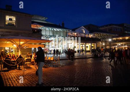 Londra, UK, 29 ottobre 2021: Mentre il crepuscolo cade a Covent Garden e nelle strade acciottolate circostanti, i turisti e gli amanti dello shopping godono di un incantesimo secco tra le docce a pioggia. I ristoranti e i ristoratori di bar, pub o ristoranti hanno spesso la scelta di sedersi all'interno o all'esterno. Le campagne pubblicitarie volte a incoraggiare le persone a visitare Londra sembrano aver attirato molte visite familiari a metà termine e Londra ha attualmente un tasso di infezioni da covid inferiore rispetto ad altre aree del paese. Le decorazioni natalizie sono già in alto nella zona centrale del mercato. Anna Watson/Alamy Live News Foto Stock