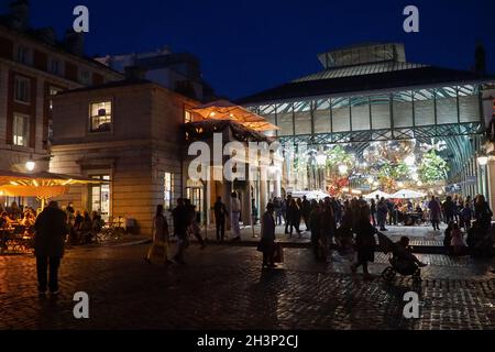 Londra, UK, 29 ottobre 2021: Mentre il crepuscolo cade a Covent Garden e nelle strade acciottolate circostanti, i turisti e gli amanti dello shopping godono di un incantesimo secco tra le docce a pioggia. I ristoranti e i ristoratori di bar, pub o ristoranti hanno spesso la scelta di sedersi all'interno o all'esterno. Le campagne pubblicitarie volte a incoraggiare le persone a visitare Londra sembrano aver attirato molte visite familiari a metà termine e Londra ha attualmente un tasso di infezioni da covid inferiore rispetto ad altre aree del paese. Le decorazioni natalizie sono già in alto nella zona centrale del mercato. Anna Watson/Alamy Live News Foto Stock