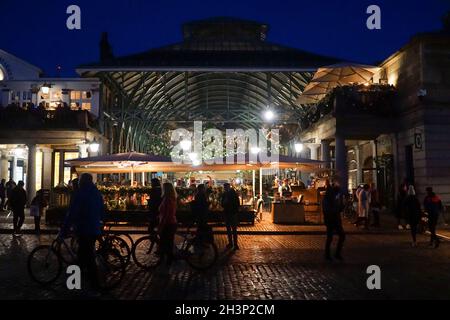 Londra, UK, 29 ottobre 2021: Mentre il crepuscolo cade a Covent Garden e nelle strade acciottolate circostanti, i turisti e gli amanti dello shopping godono di un incantesimo secco tra le docce a pioggia. I ristoranti e i ristoratori di bar, pub o ristoranti hanno spesso la scelta di sedersi all'interno o all'esterno. Le campagne pubblicitarie volte a incoraggiare le persone a visitare Londra sembrano aver attirato molte visite familiari a metà termine e Londra ha attualmente un tasso di infezioni da covid inferiore rispetto ad altre aree del paese. Le decorazioni natalizie sono già in alto nella zona centrale del mercato. Anna Watson/Alamy Live News Foto Stock