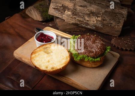 Hamburger di manzo fresco con salsa di ciliegia in una ciotola di salsa, lattuga fresca con panna di piombo adagiato accanto con logge di legno come decorazione Foto Stock