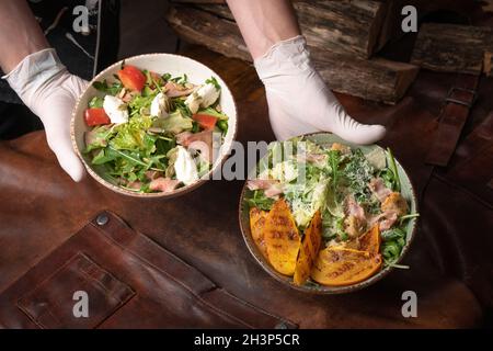 Due ciotole di insalata di verdure con salmone, mozzarella e fette di frutta alla griglia si erige su un tavolo coperto da un leathe Foto Stock