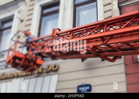 Piattaforma di lavoro aerea veicolo durante la decorazione della facciata, ascensore telescopico arancione sul cantiere, noleggio AWP lavoro nelle strade della città, motore Foto Stock