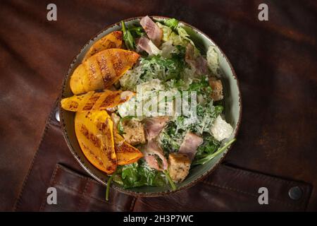 Vista dall'alto di una ciotola di insalata fresca con salmone, mozzarella e fette di frutta grigliate su un tavolo coperto da un litro Foto Stock