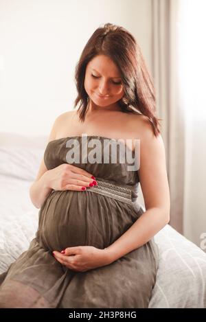 Donna incinta in vestito contro la finestra Foto Stock