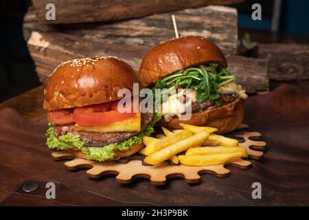 Gustosi hamburger di manzo fresco artigianale con patatine fritte, uno con noci fritte sono serviti su una parte decorativa in legno di una mecc semplice Foto Stock